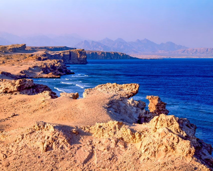 RED SEA Coastal landscape with rocky formations and calm blue waters under a pastel sky.
